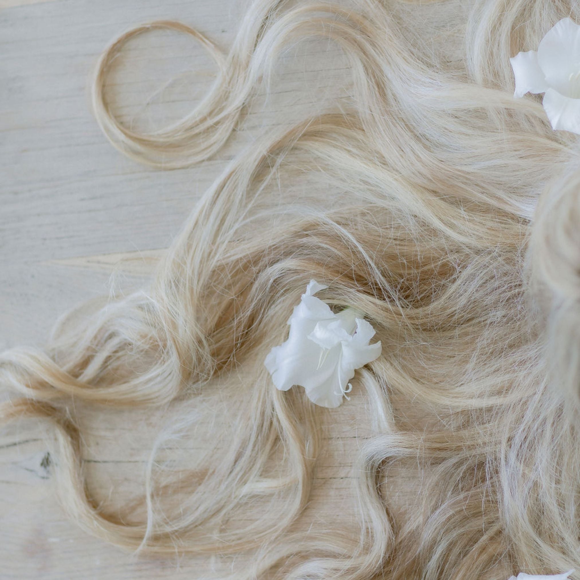 Blonde hair extensions with a white flower accessory on a light wooden surface