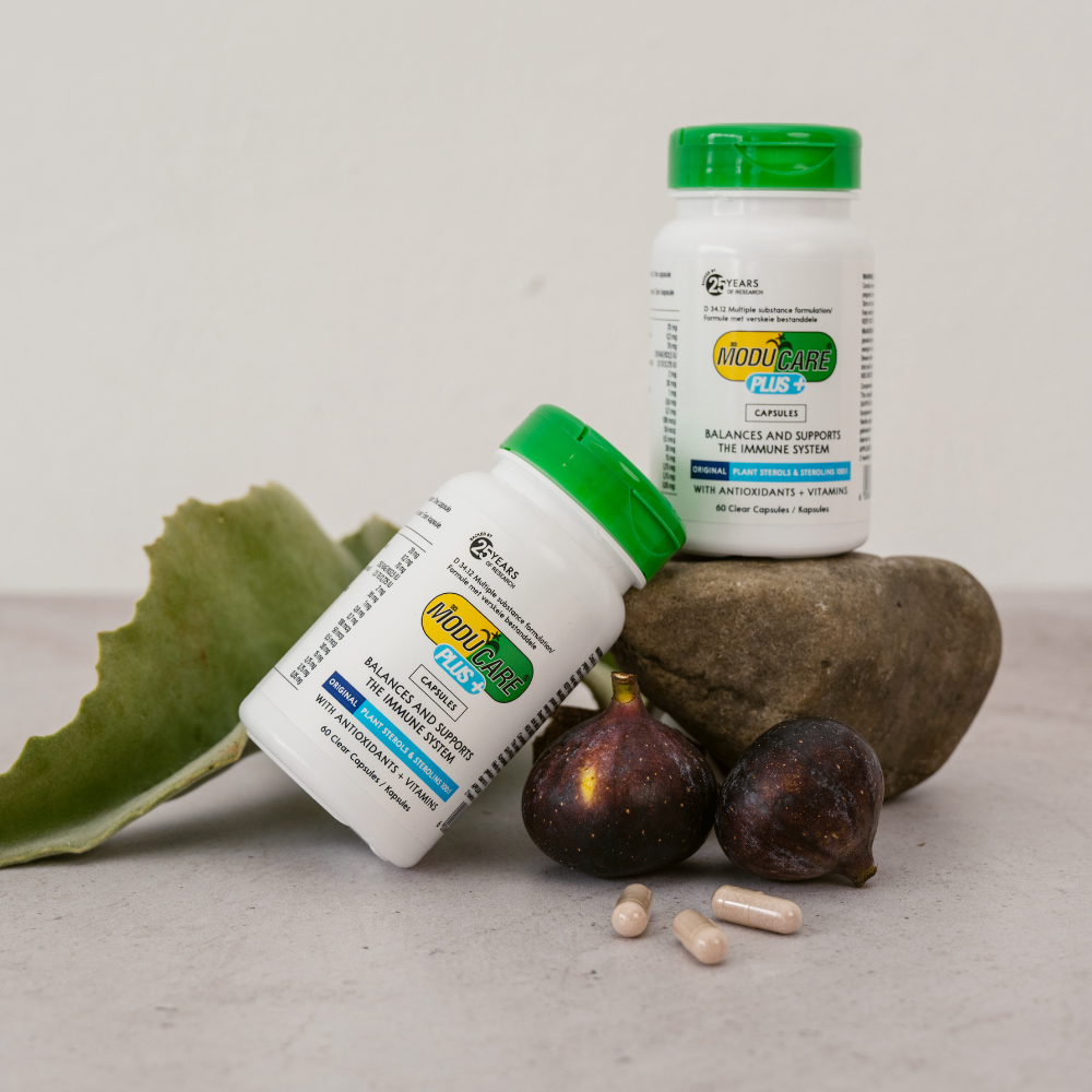 Supplement bottle labeled 'Moducare Plus' on a stone surface with figs and herbs.