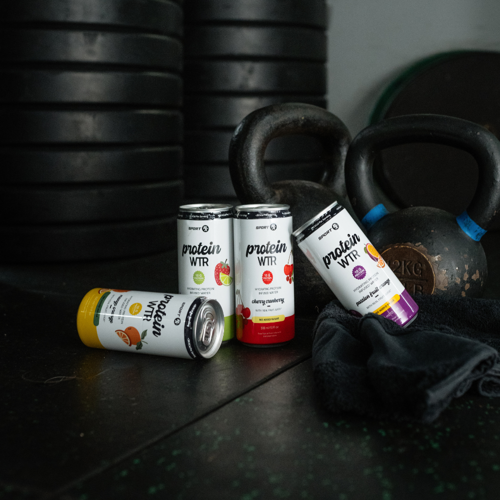 Protein WTR containers and a kettlebell on a gym floor with weights in the background