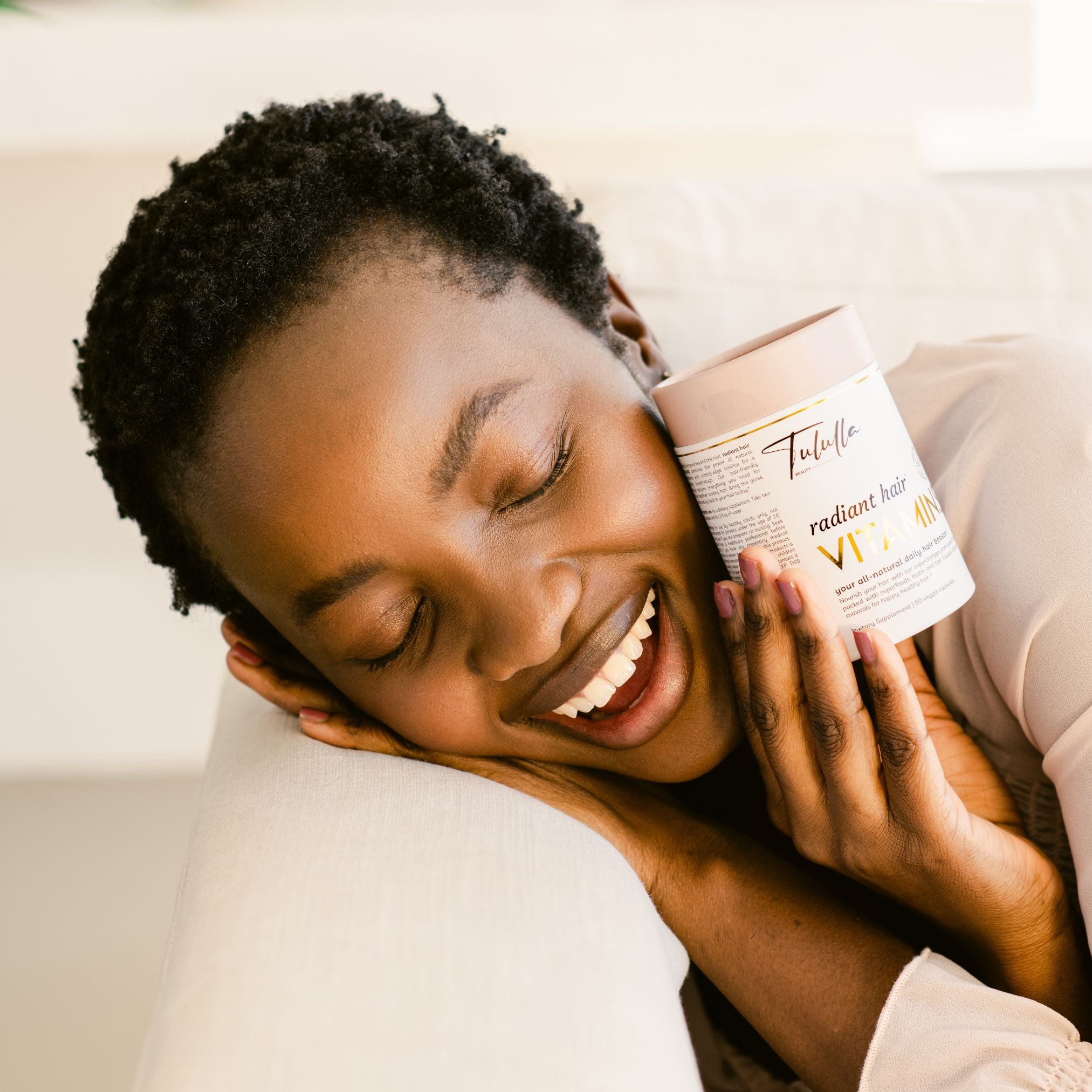 Woman holding a product with a visible brand logo, smiling and lying on a couch.