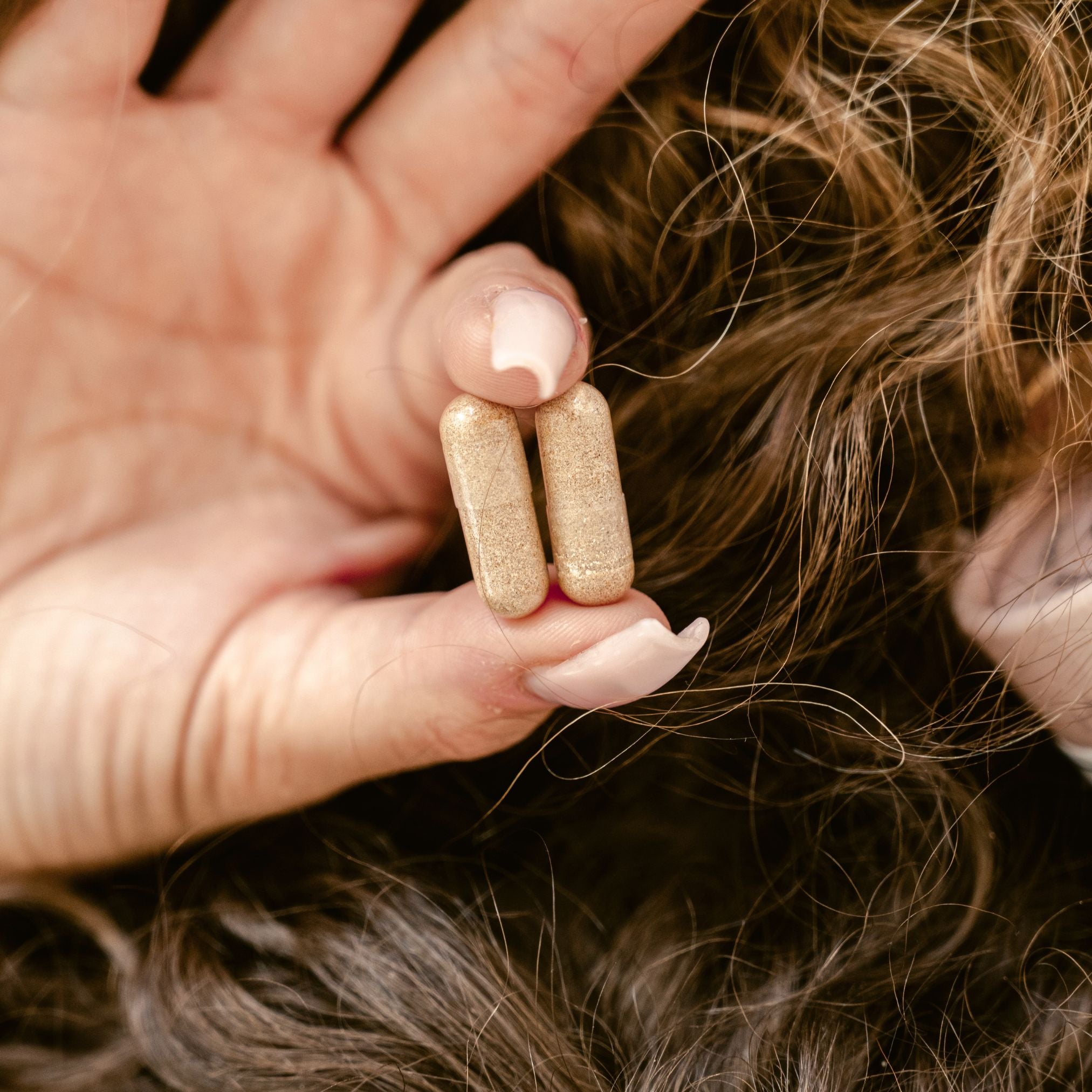 Hand holding two gold-colored hair extensions against a blurred background