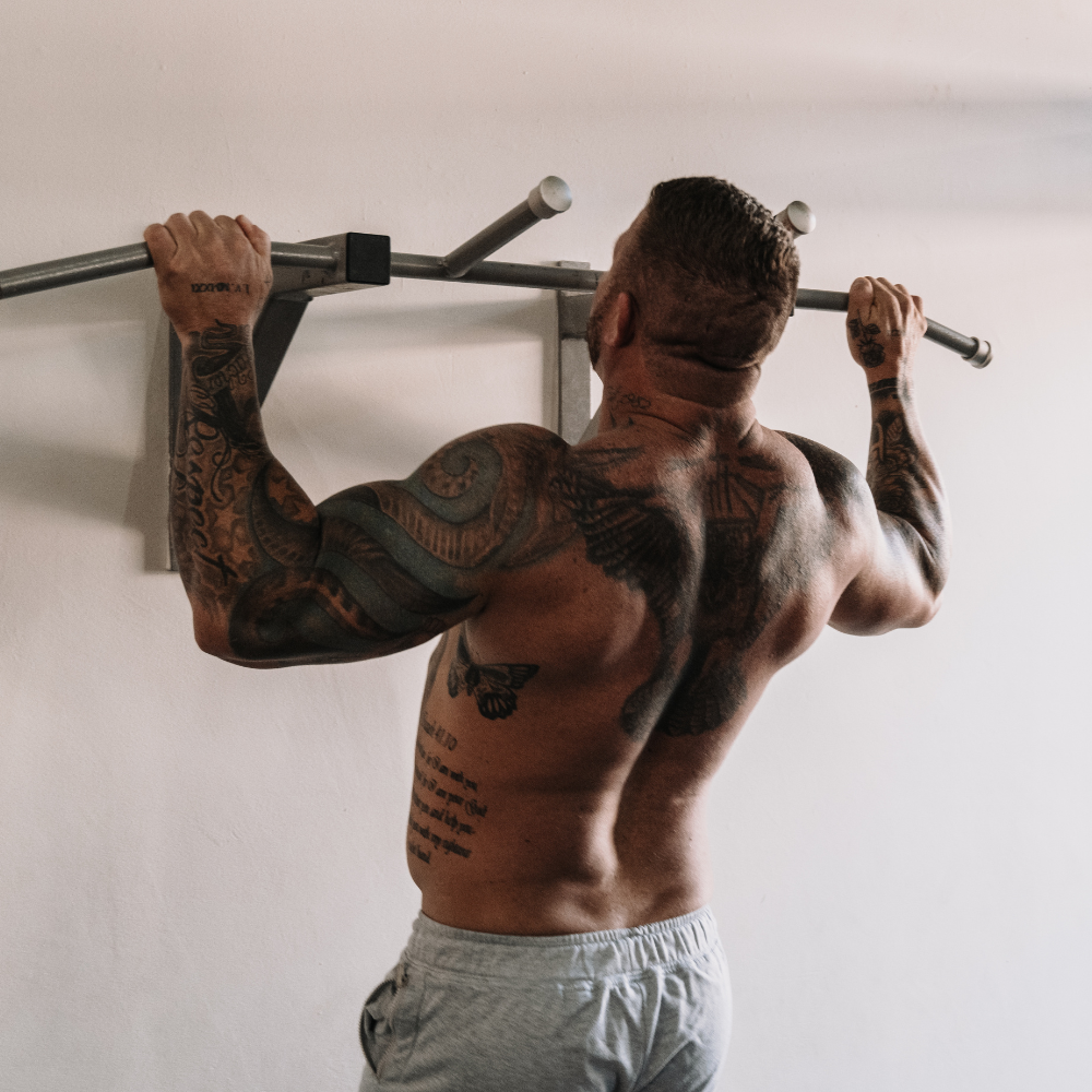 Man with tattoos doing pull-ups on a bar against a white wall