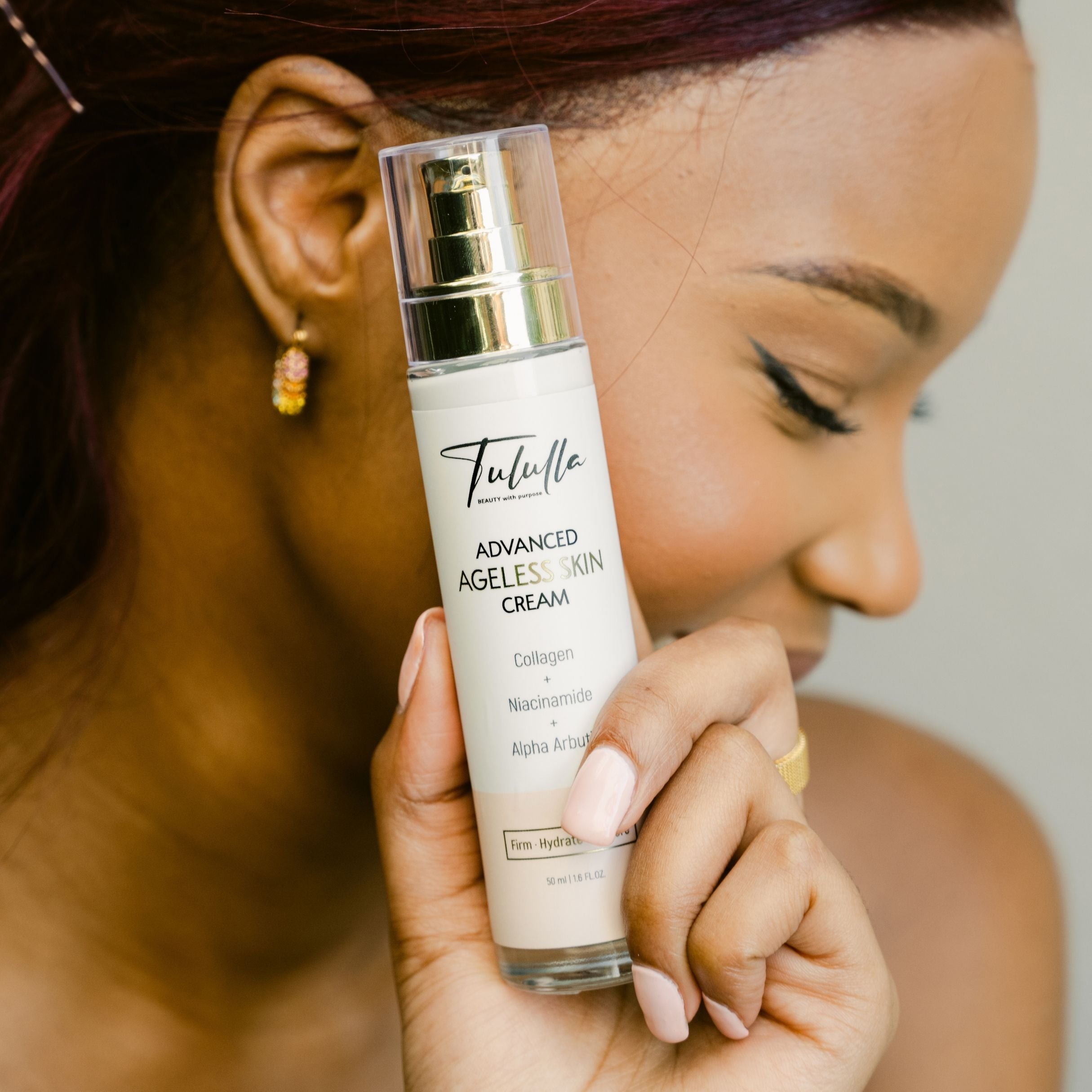 Woman holding a bottle of Tulula Advanced Ageless Skin Cream close to her face.